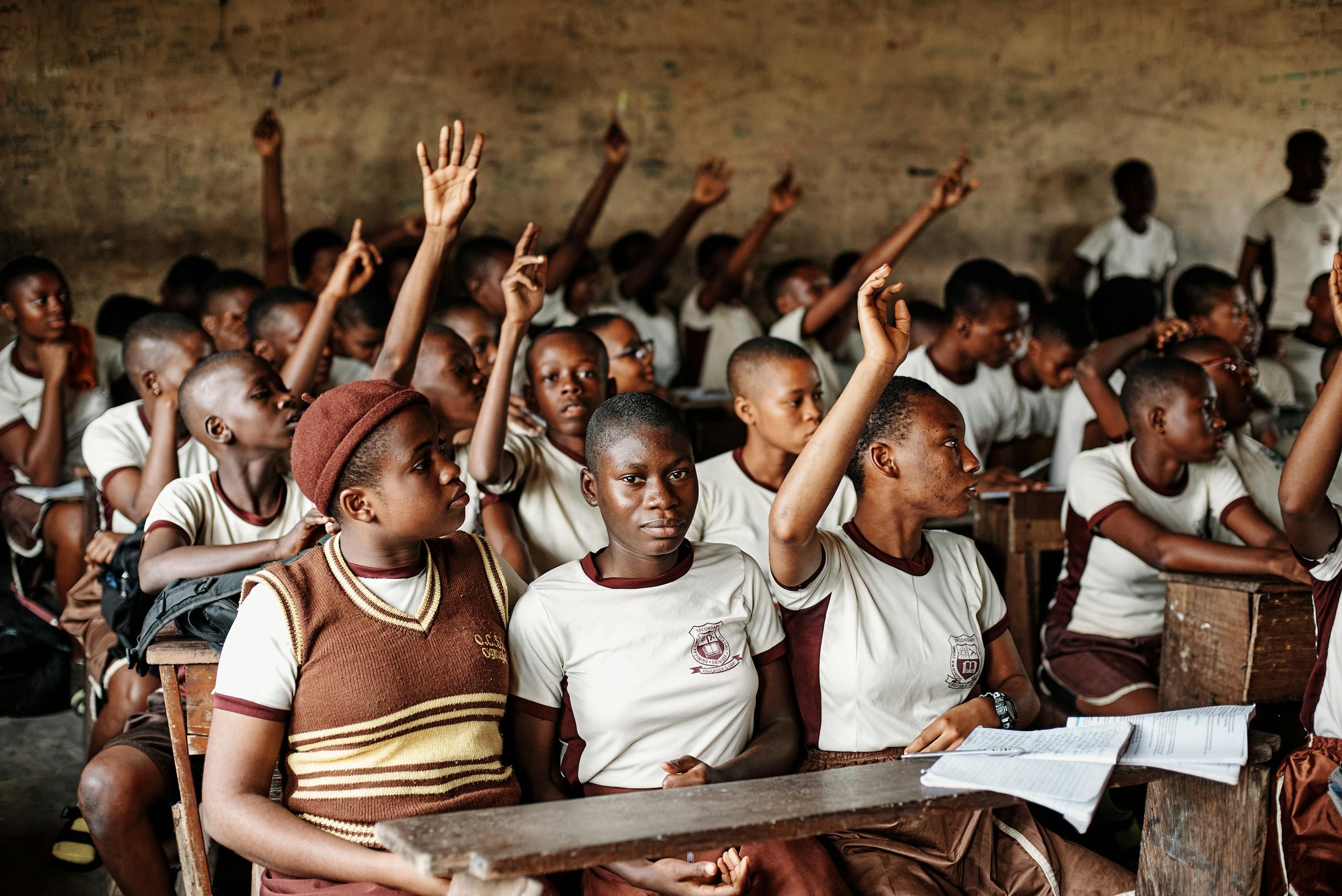 A group of attentive African students raising hands in a classroom in Nigeria.