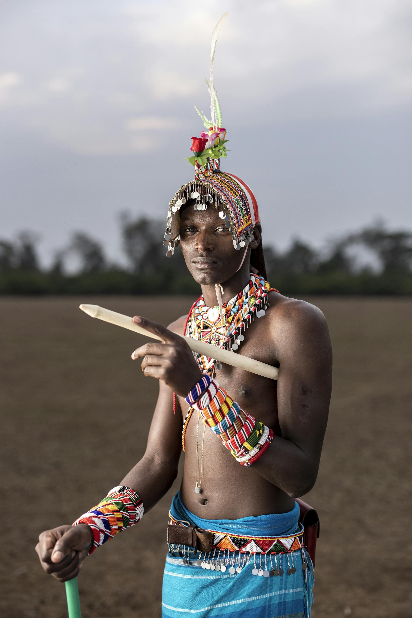 A Masai man stands proudly in traditional attire set against the scenic landscape of Kenya.