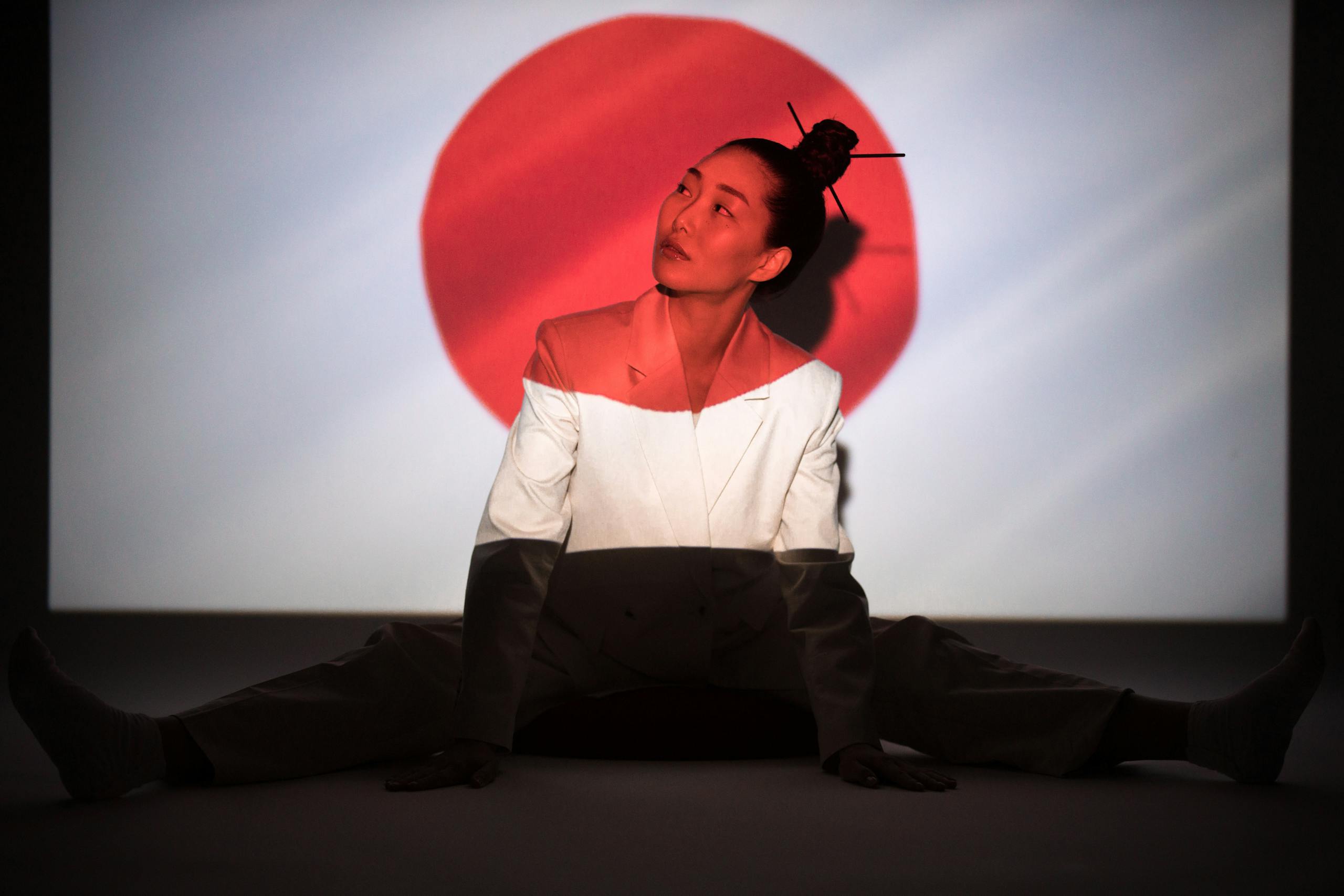 Asian woman poses with Japanese flag projection, embodying cultural symbolism.