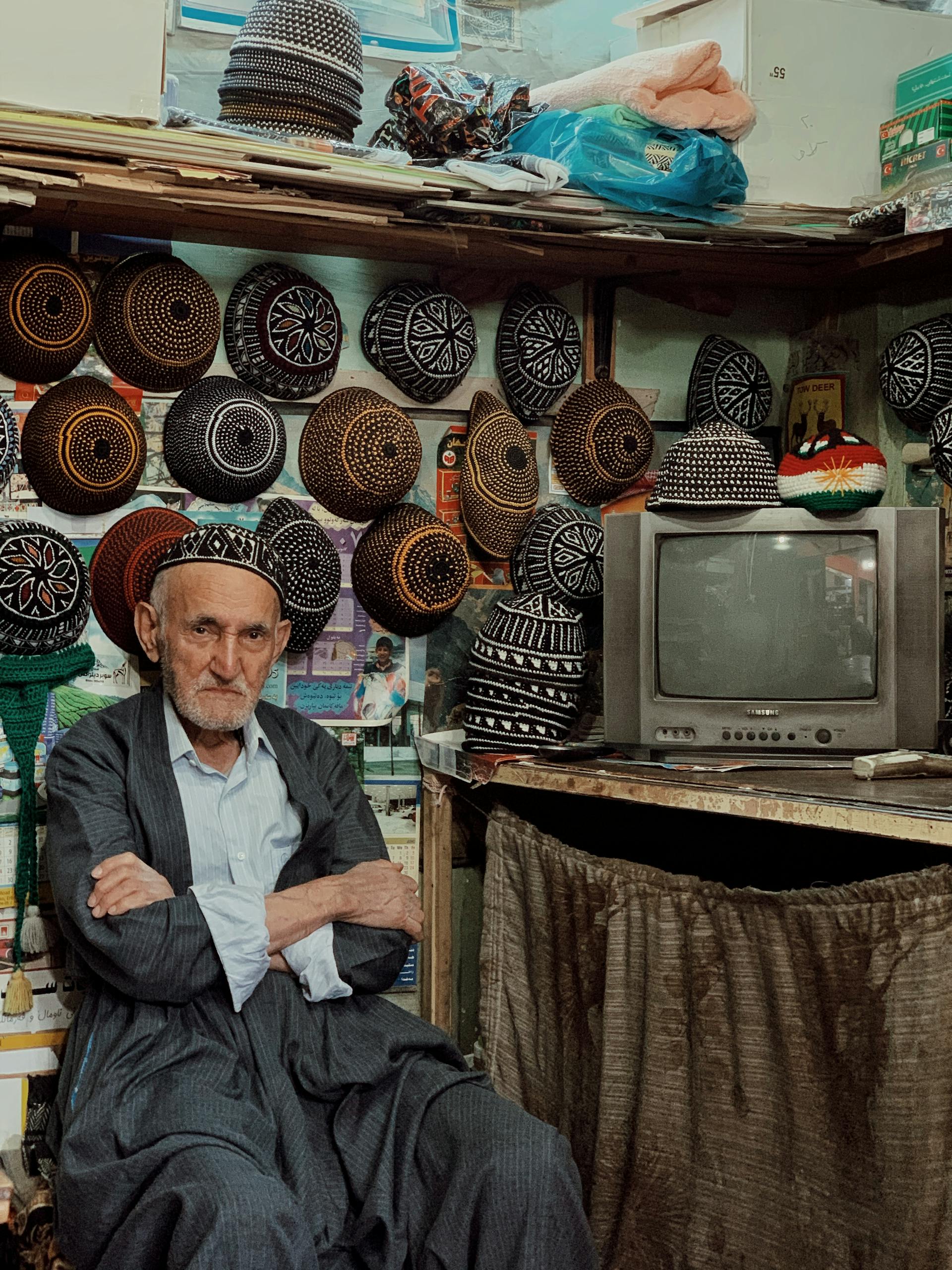 Senior man in Iraq shop with traditional hats and vintage TV.