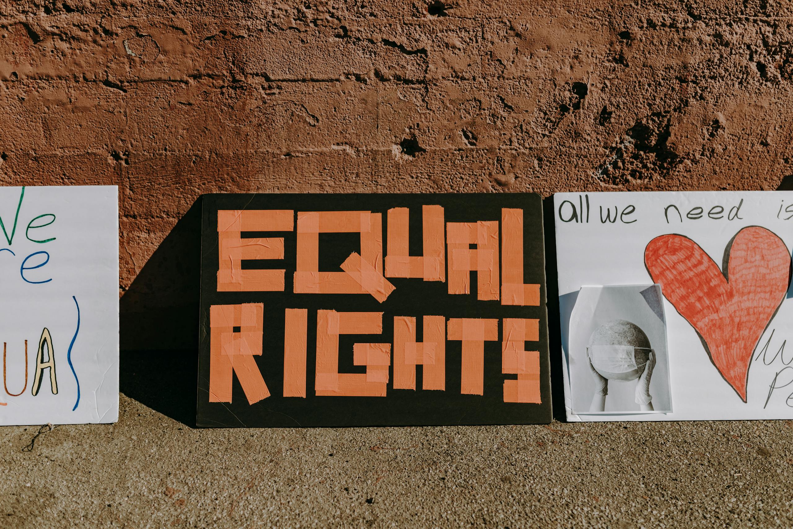 Three protest signs promoting equal rights and activism displayed on a textured wall.